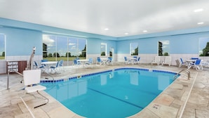 An indoor swimming pool with clear blue water, surrounded by lounge chairs and tables, and large windows offering a view of the outdoors. - Holiday Inn Express & Suites Bloomington - Normal by IHG (Normal)