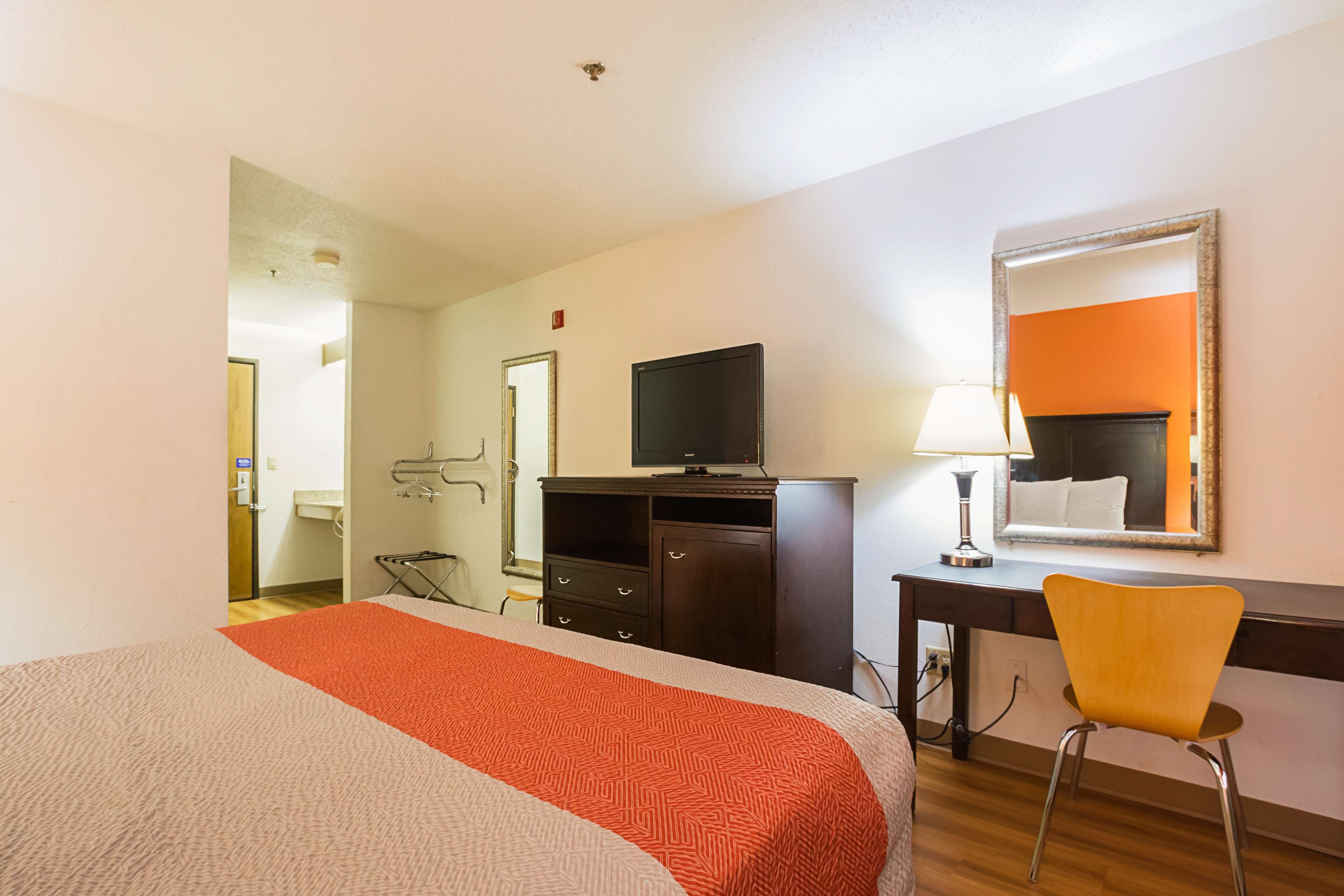 Una habitación de hotel con una cama, un escritorio con televisor, una silla y un espejo en la pared.