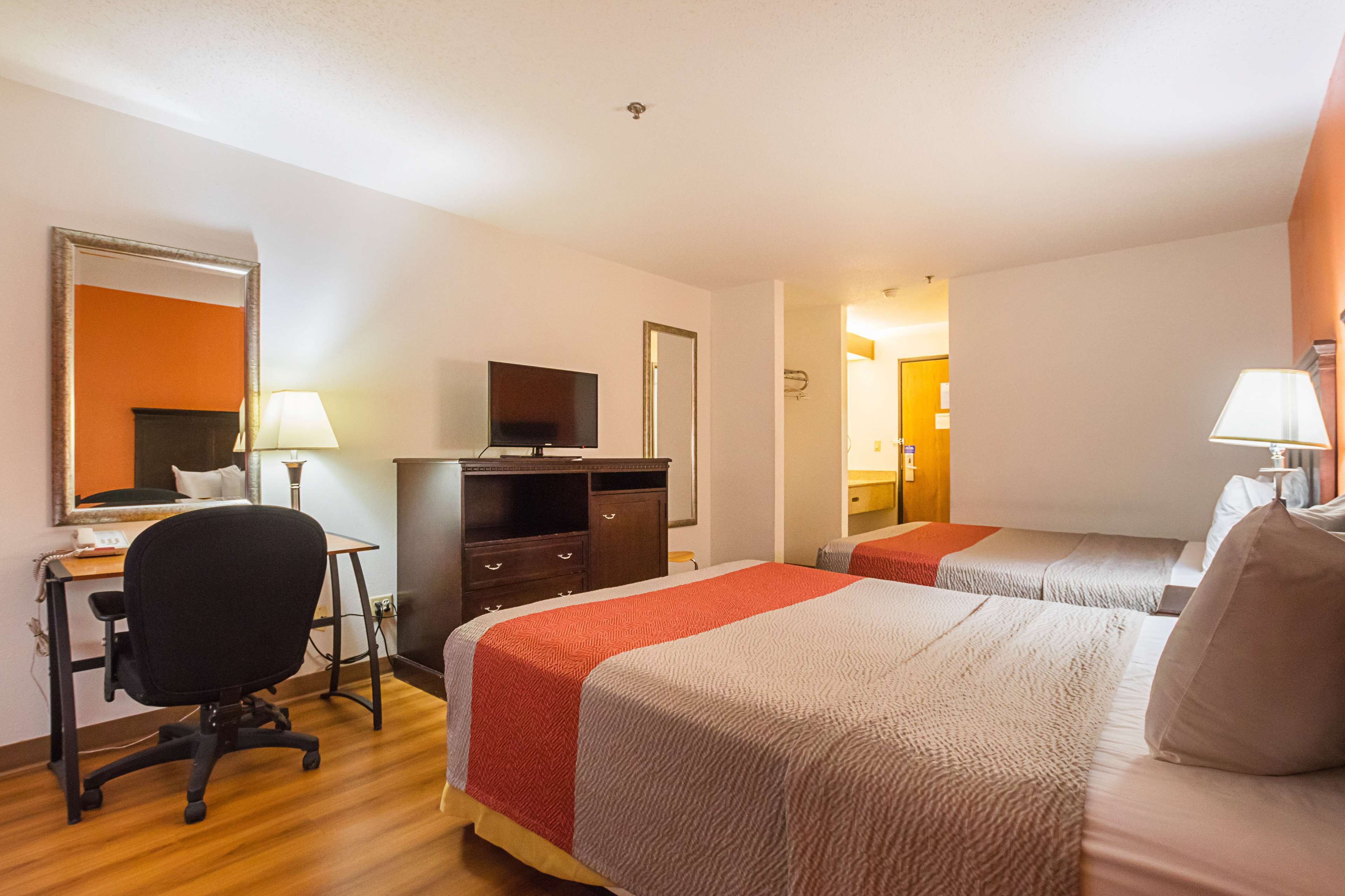 A hotel room with two beds, a desk, a chair, a television, and a mirror.