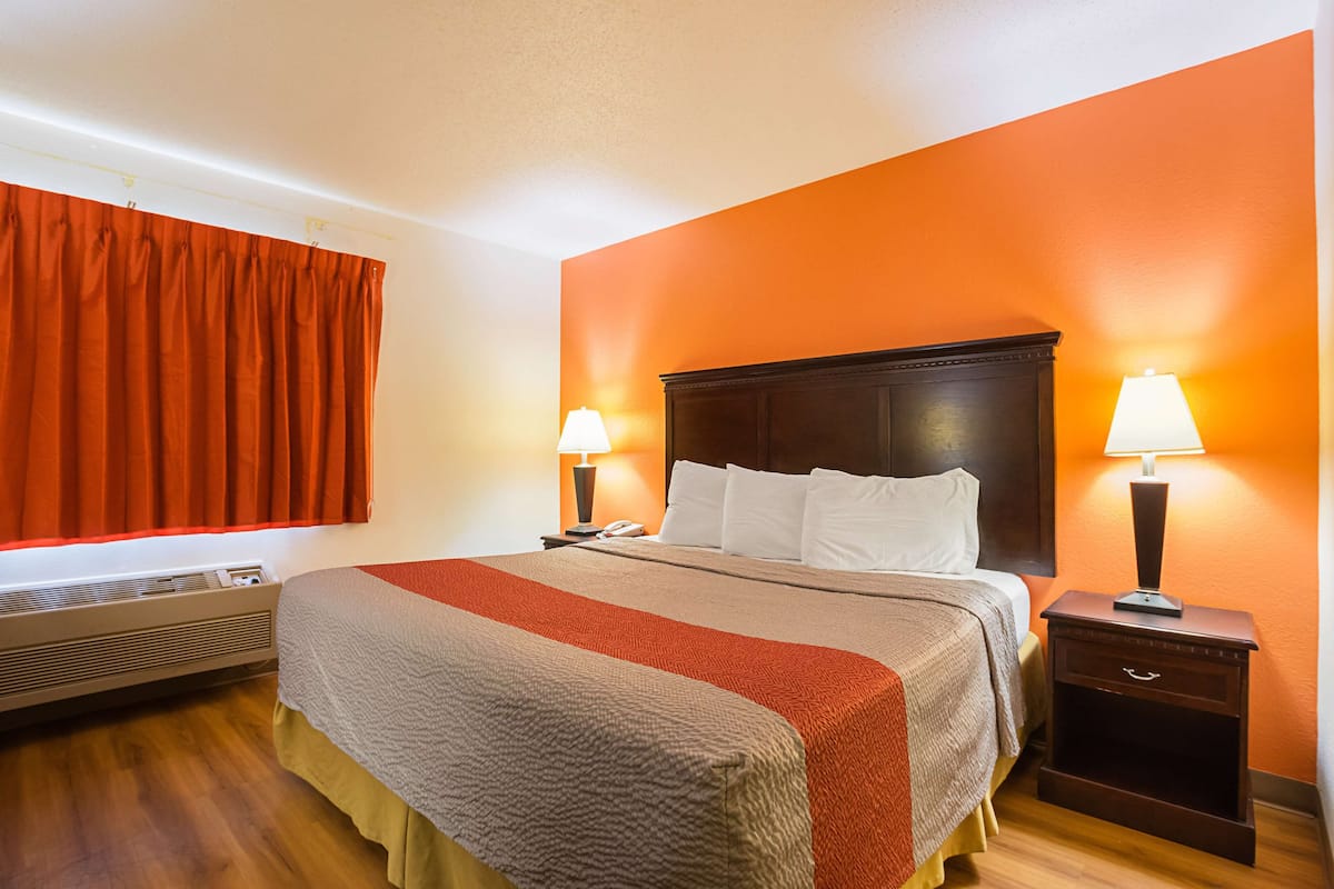 Ein Hotelzimmer mit Bett, zwei Nachttischlampen, einem Nachttisch und einem Fenster mit Vorhängen.