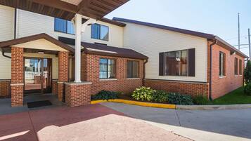 A two-story building with a brick facade, a covered entrance, and a small garden area.