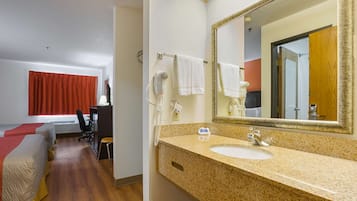 A hotel room with a bed, a desk, a chair, a bathroom with a sink and mirror, and a red curtain.