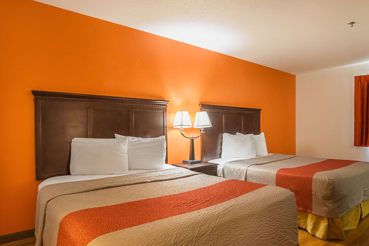 Ein Hotelzimmer mit zwei Betten, einem Nachttisch mit Lampen und einer orangefarbenen Wand.