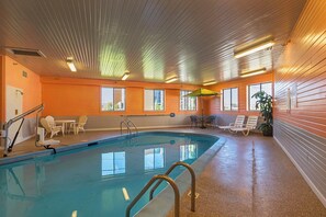 An indoor swimming pool with a clear view of the pool area, including a pool ladder, lounge chairs, and a table with chairs. - Motel 6 Waterloo, IA - Crossroads Mall - Cedar Falls (Waterloo)