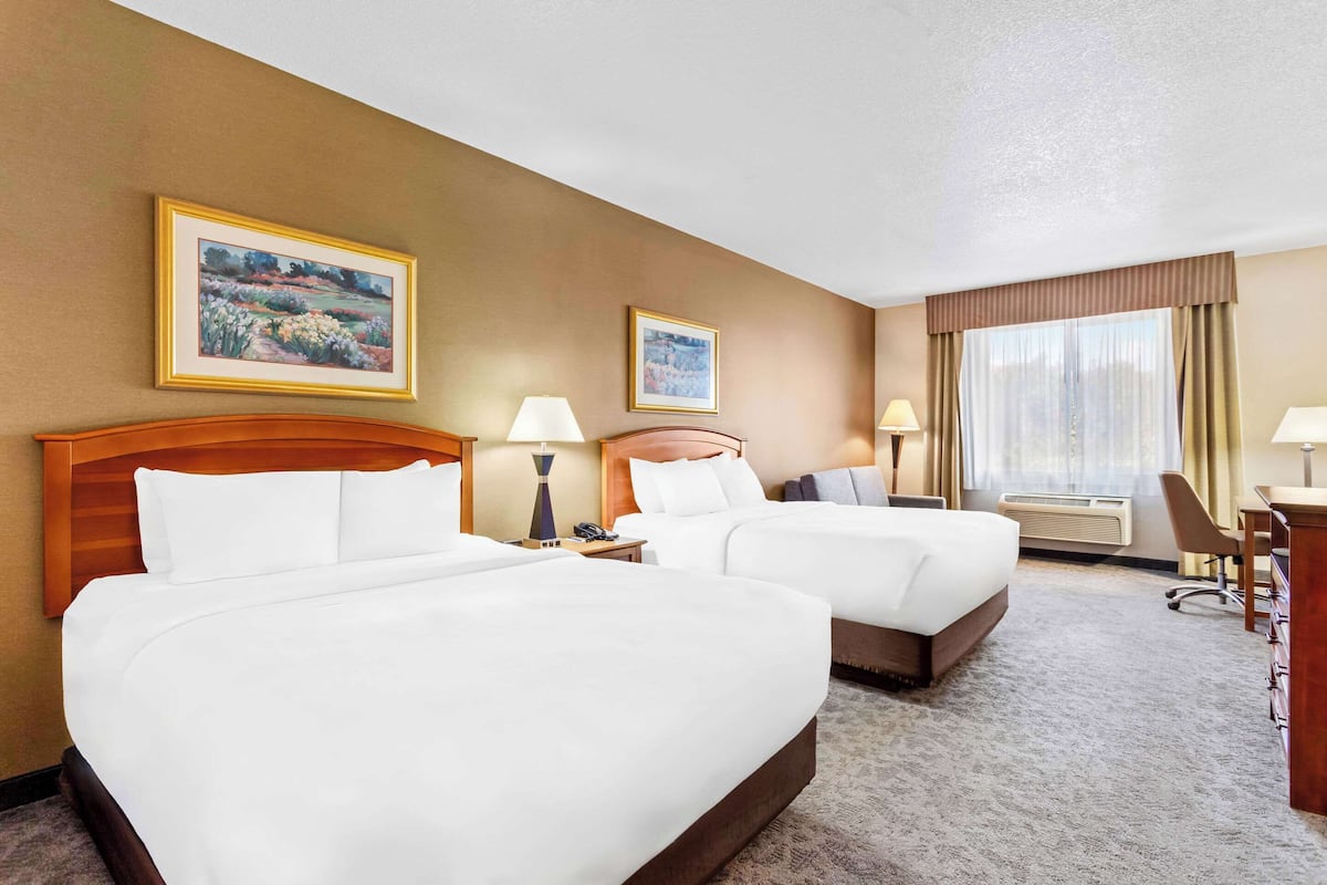 A hotel room with two beds, a desk, a chair, and two paintings on the walls.