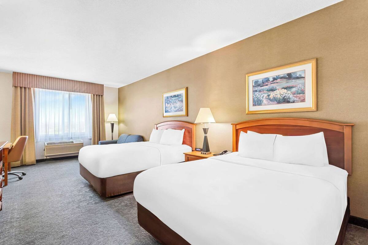 A hotel room with two beds, a desk, a chair, and two paintings on the wall.