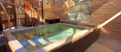 Un bain à remous avec un mur en bois et une fontaine en pierre.