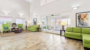 Un hall d’entrée spacieux, doté de sièges confortables recouverts d’un tissu vert, d’une table basse et d’une grande porte vitrée donnant sur un balcon.