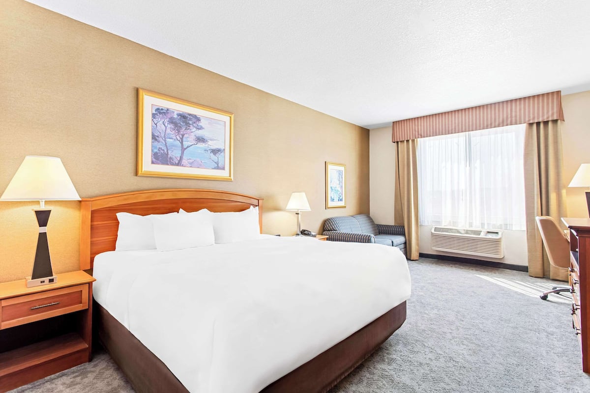 A hotel room with a large bed, two bedside tables with lamps, a chair, a desk, and a large window with curtains.