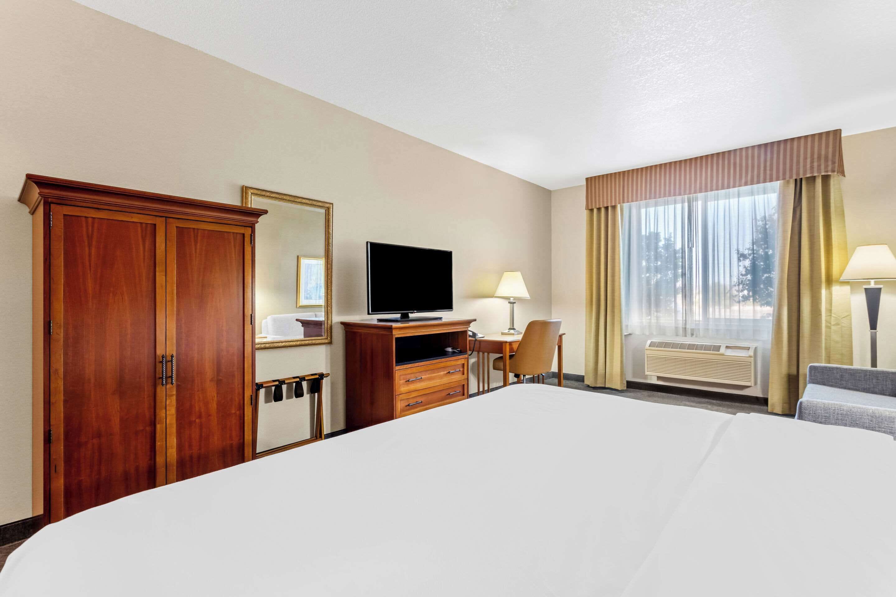 Camera d'albergo con un letto grande, una televisione, una scrivania con una sedia, un armadio e una finestra con tende.