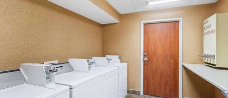 A laundry area with white washers and dryers, a wooden door, and a shelf with soap and bleach.