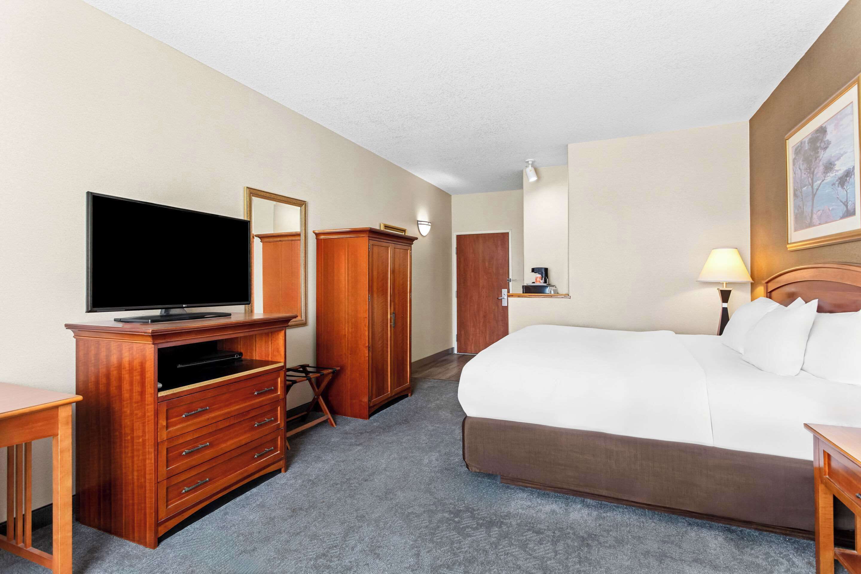 A hotel room with a bed, a television, a wardrobe, and a desk.