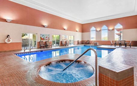 A swimming pool with a hot tub, surrounded by outdoor seating and a stone wall.