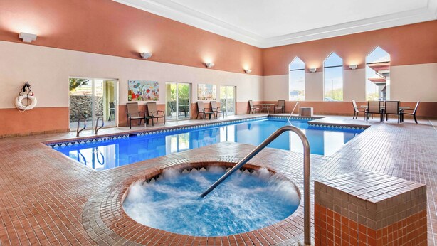Une piscine avec un jacuzzi, entourée d’un espace de détente extérieur et d’un mur en pierre.