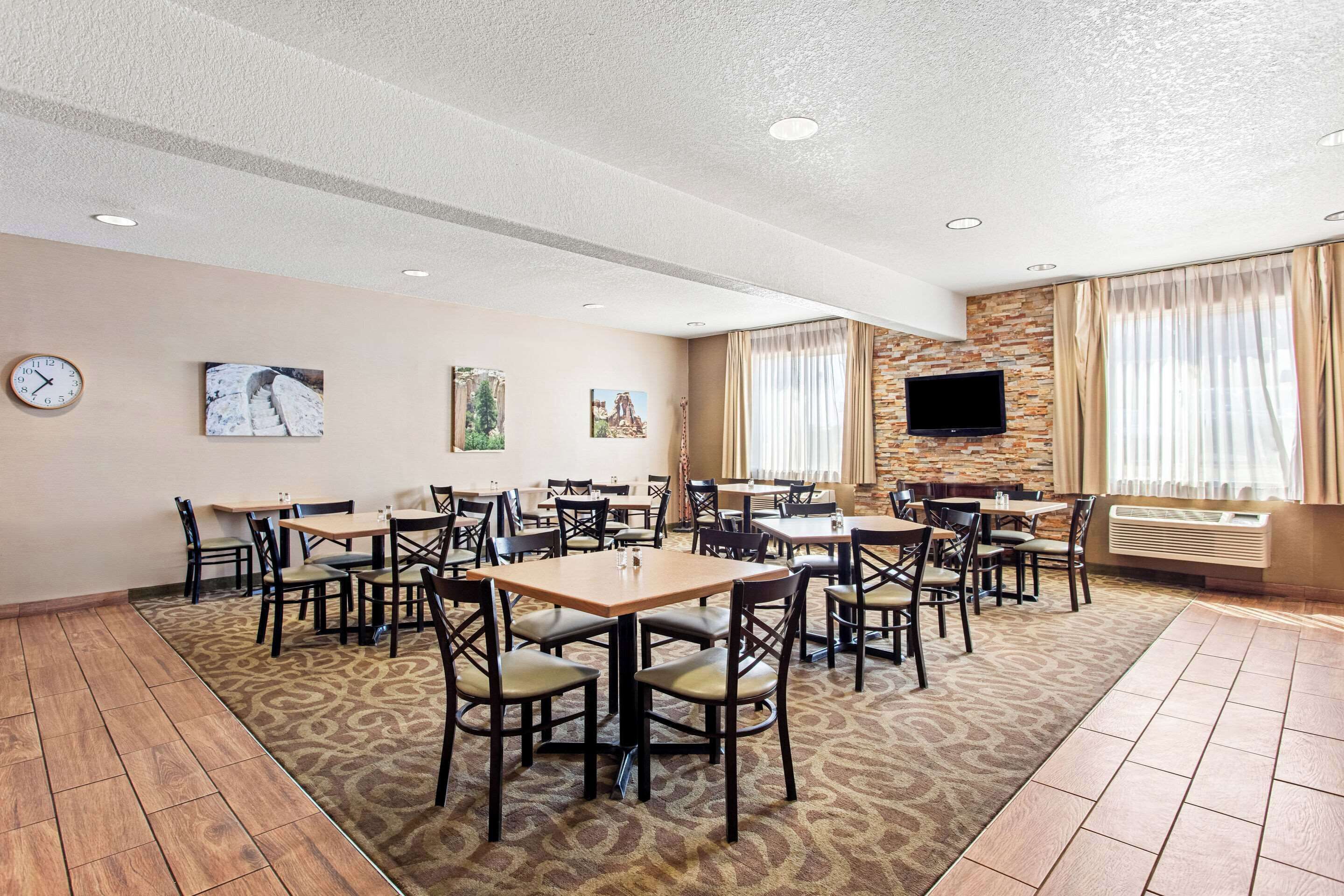 A spacious dining area with multiple tables and chairs, a clock on the wall, and a television mounted on the wall.