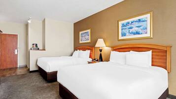 A hotel room with two beds, a wooden headboard, a bedside table with a lamp, and two framed pictures on the wall.