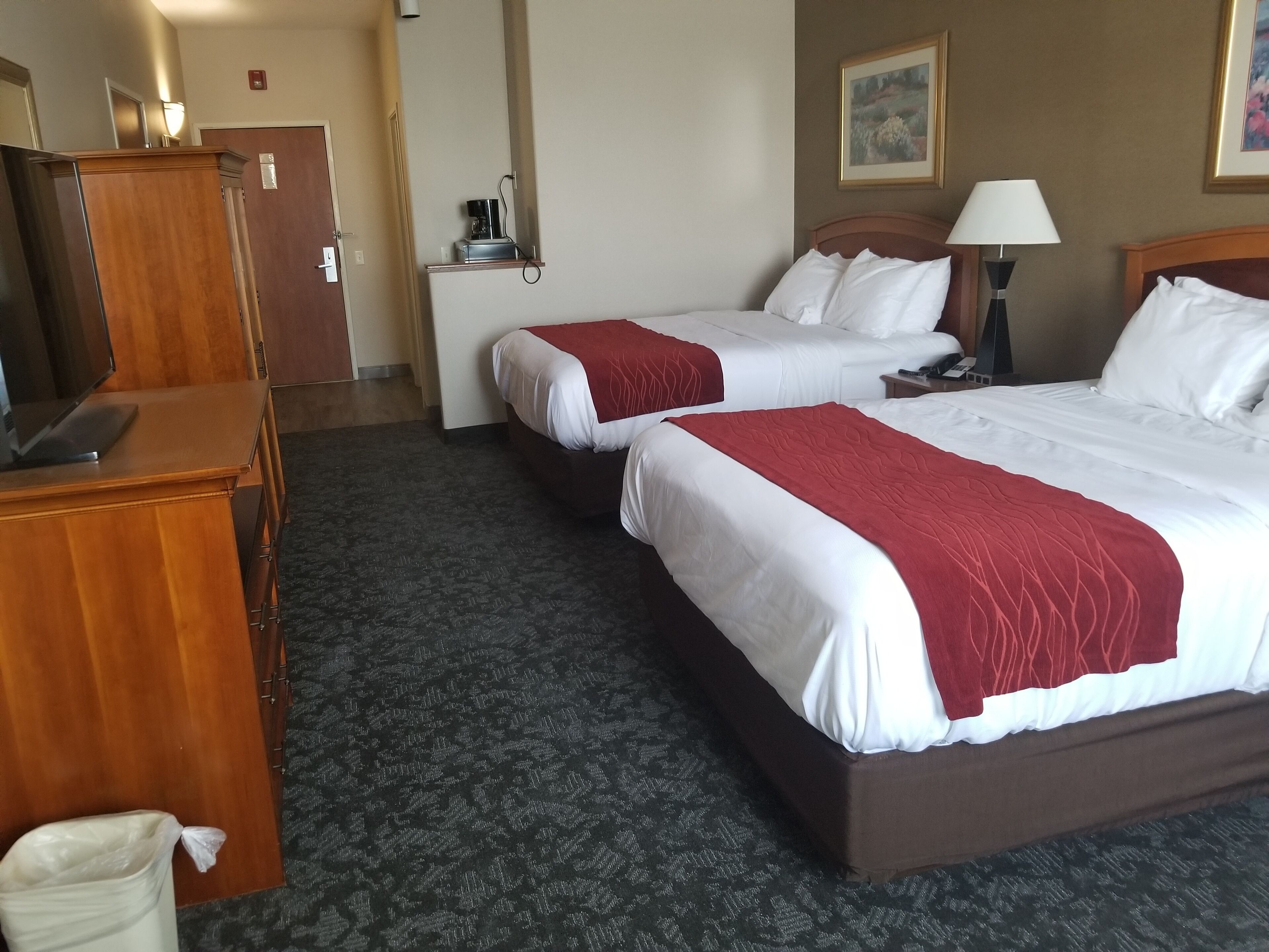A hotel room with two beds, a desk, a chair, a lamp, and a painting on the wall.