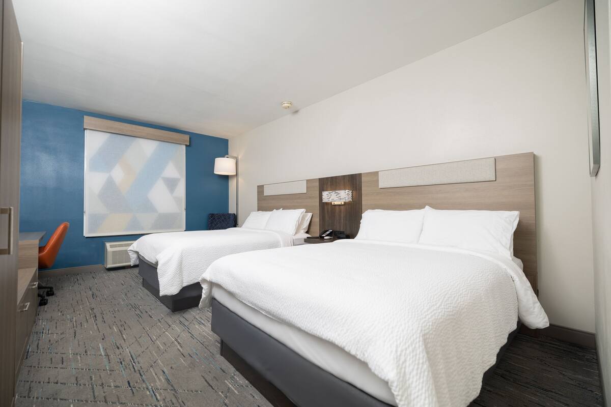 A hotel room with two beds, a blue accent wall, and a modern design.