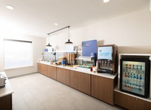 A modern coffee station with a self-serve coffee machine, a yogurt dispenser, and a variety of snacks.