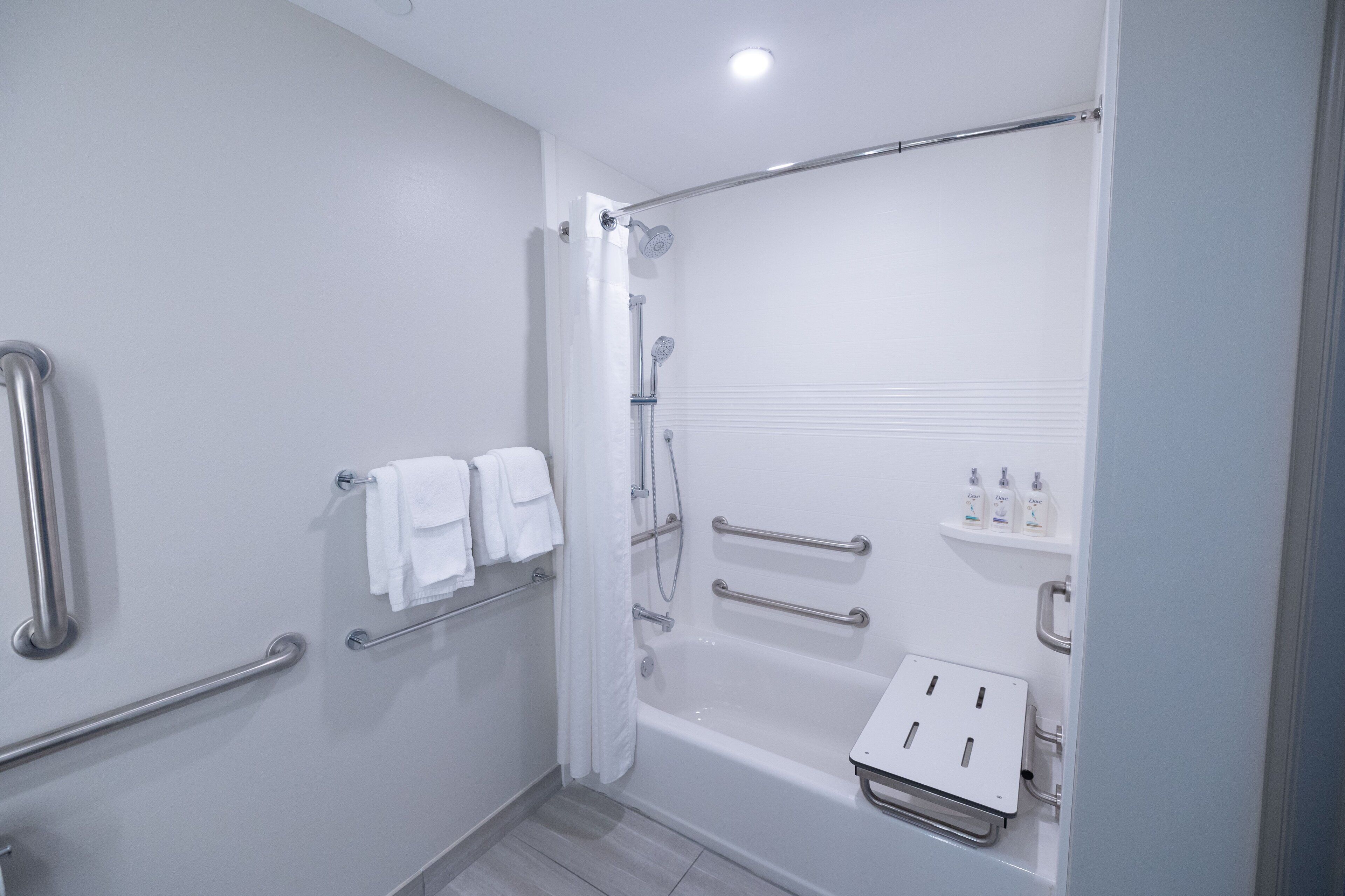 A modern bathroom with a walk-in shower, grab bars, a bathtub, and a shelf with toiletries.