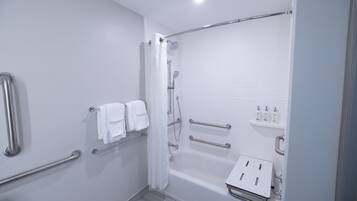 Un baño moderno con ducha a nivel, barras de apoyo, bañera y un estante con artículos de aseo.