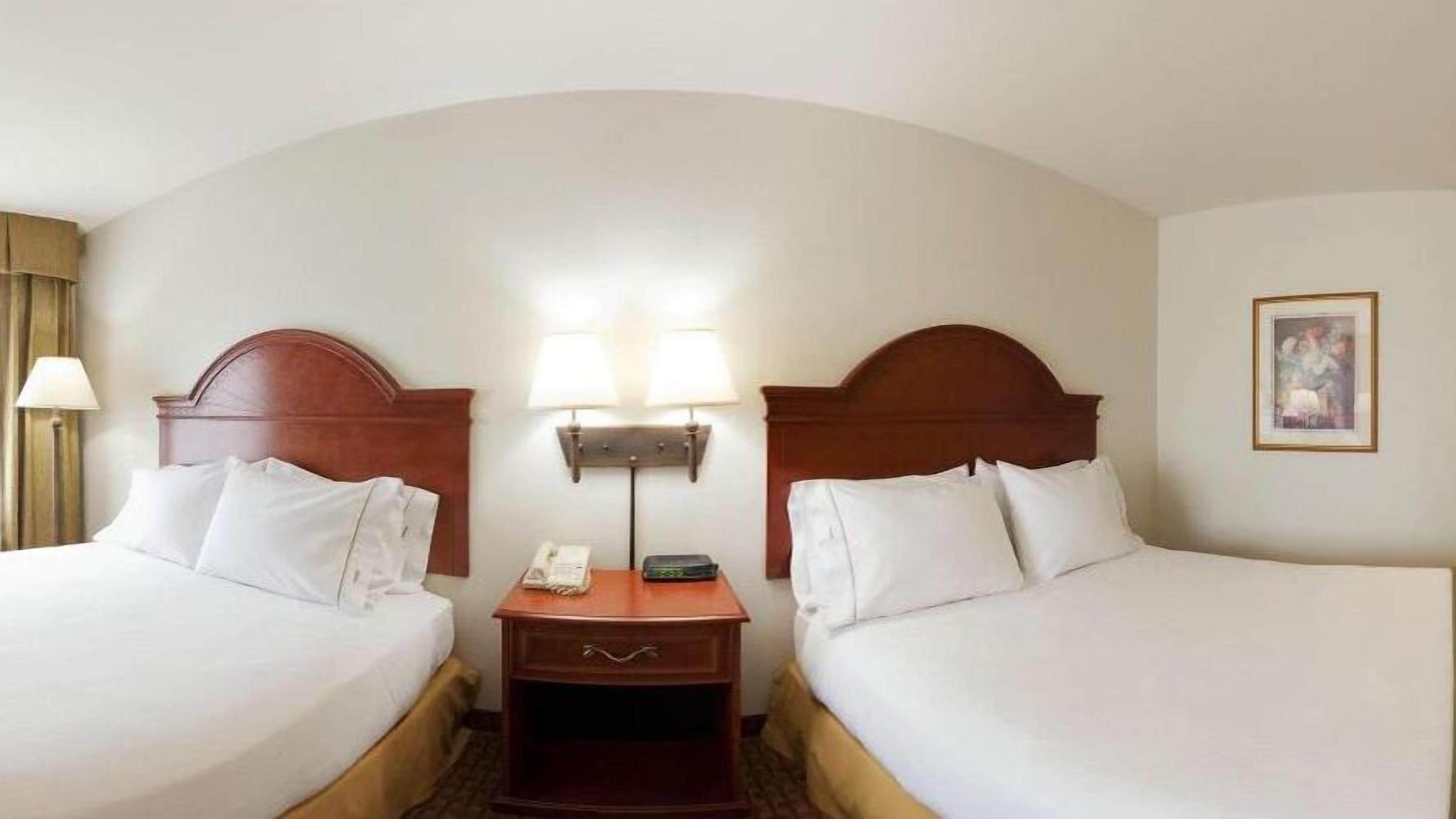 A hotel room with two beds, a nightstand with a lamp, and a painting on the wall.