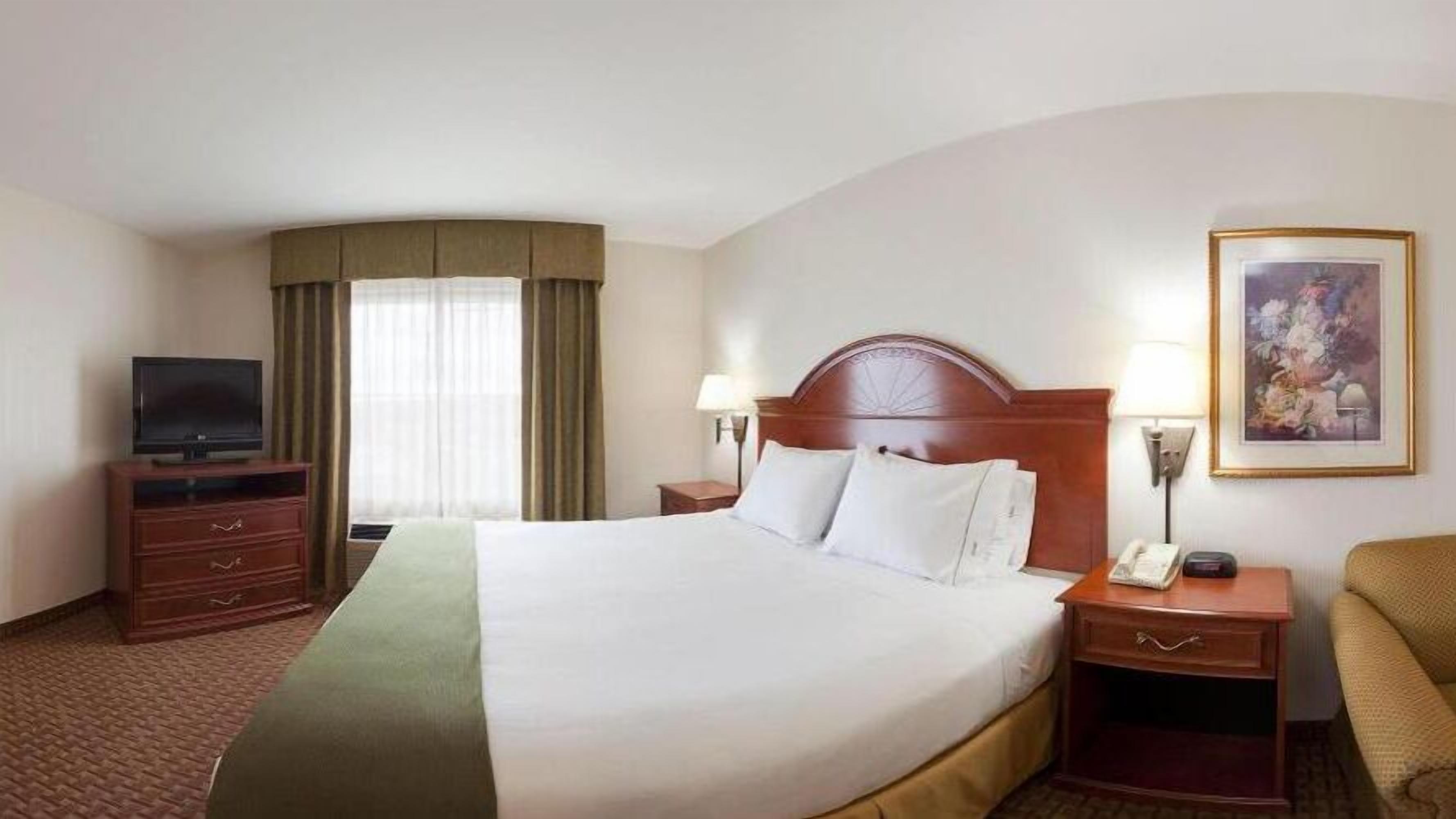 A hotel room with a large bed, a television, a desk with a lamp, and a painting on the wall.