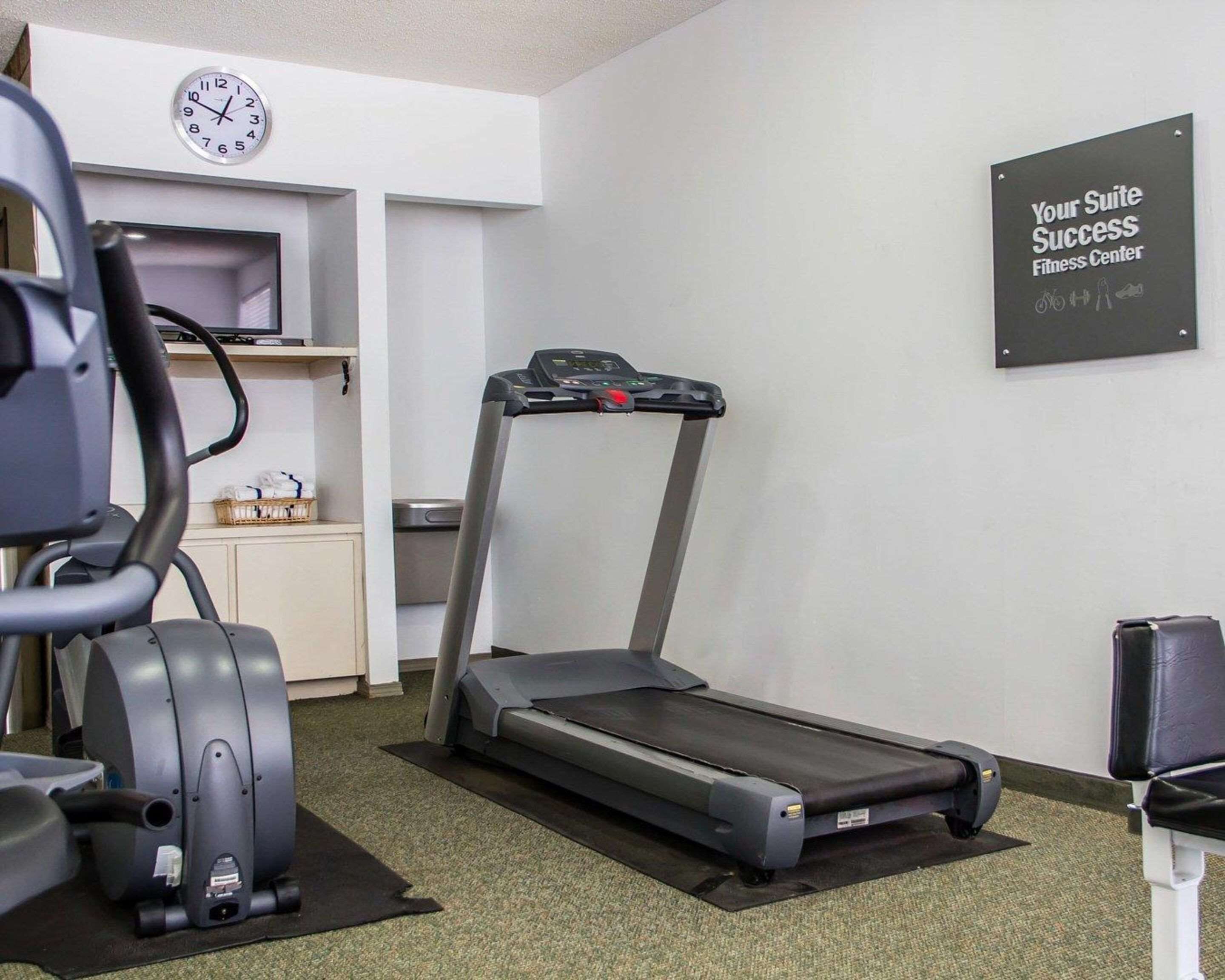 Un gimnasio con cinta de correr, elíptica y un reloj de pared.