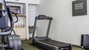 Un gimnasio con cinta de correr, elíptica y un reloj de pared.