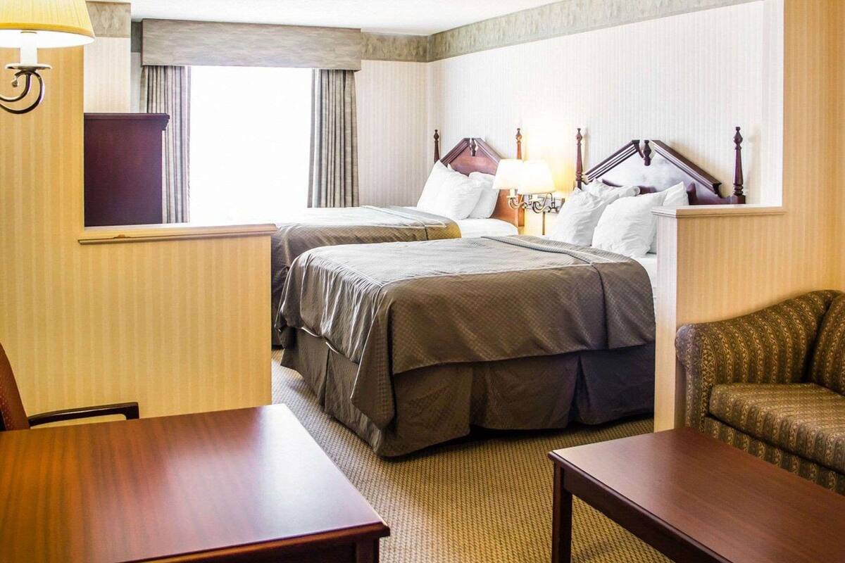 Une chambre d’hôtel avec deux lits, un bureau, une chaise, une lampe et une fenêtre avec des rideaux.