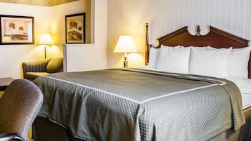 A hotel room with a large bed, two bedside lamps, a wooden headboard, and a chair.