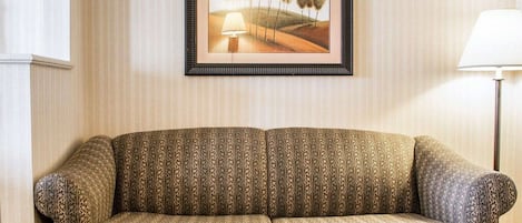 A sofa with a patterned fabric, a framed picture on the wall, and a lamp to the right.