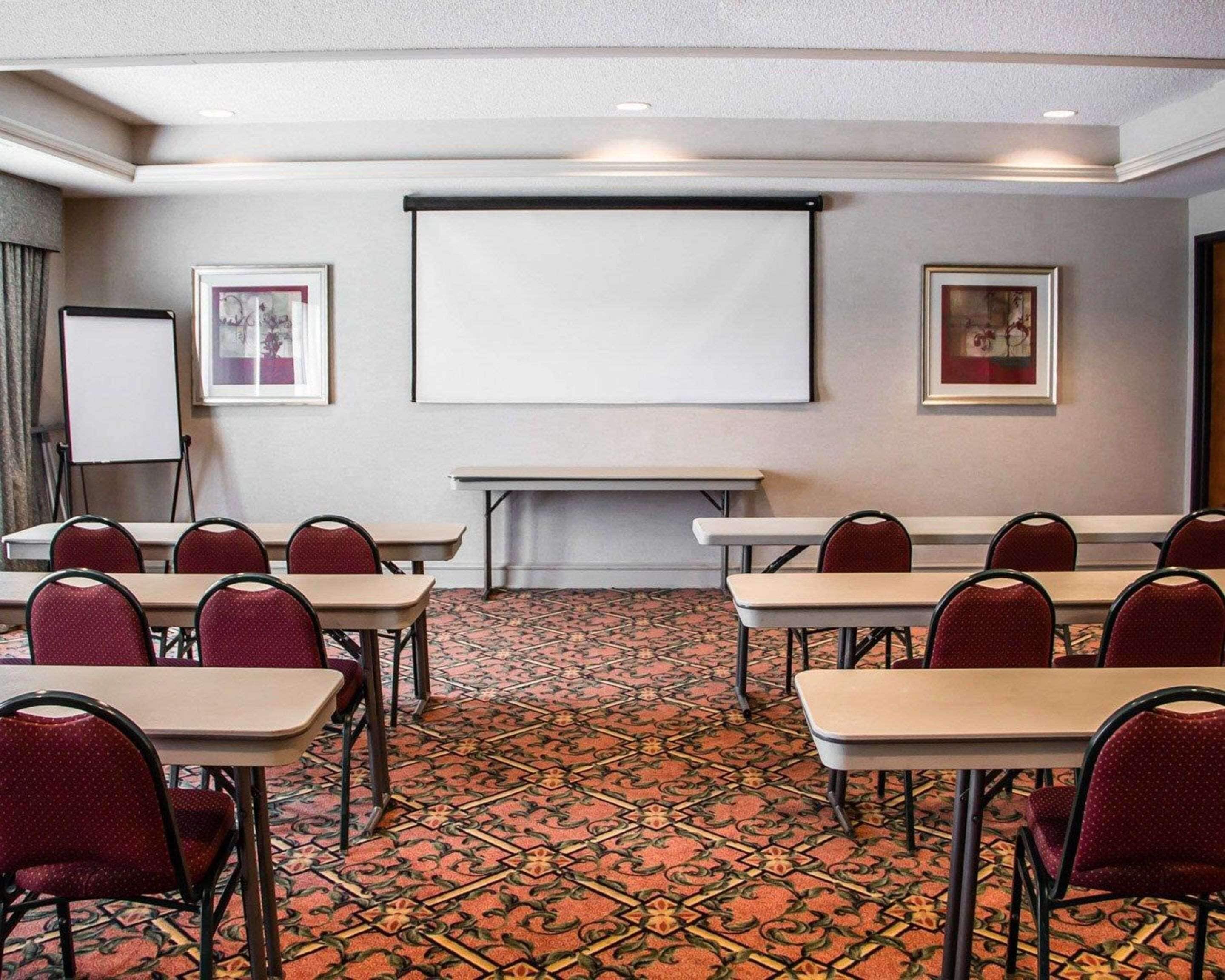 A conference room with a carpeted floor, multiple tables, and chairs. There is a whiteboard and a projector screen on the wall.