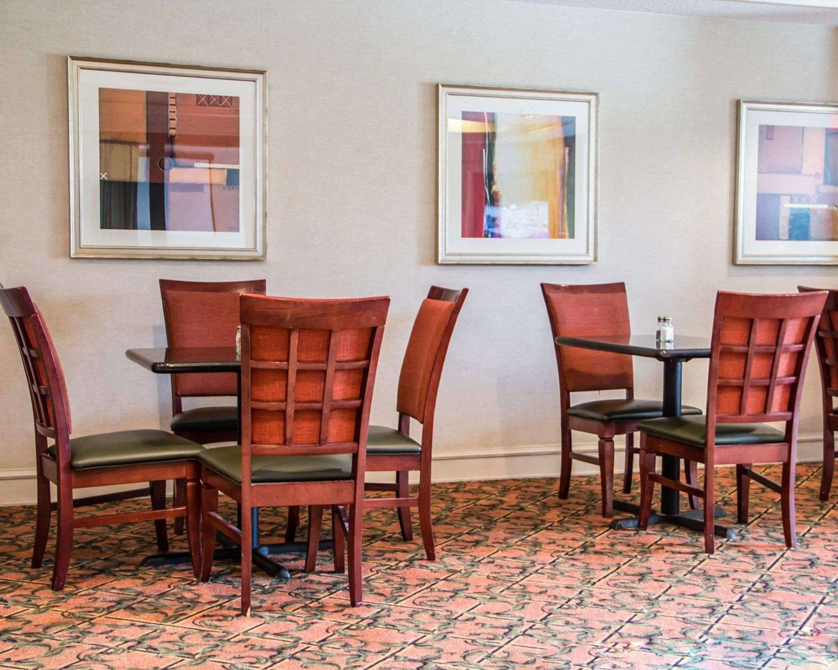 A dining area with wooden chairs and tables, framed artwork on the walls, and a patterned carpet.