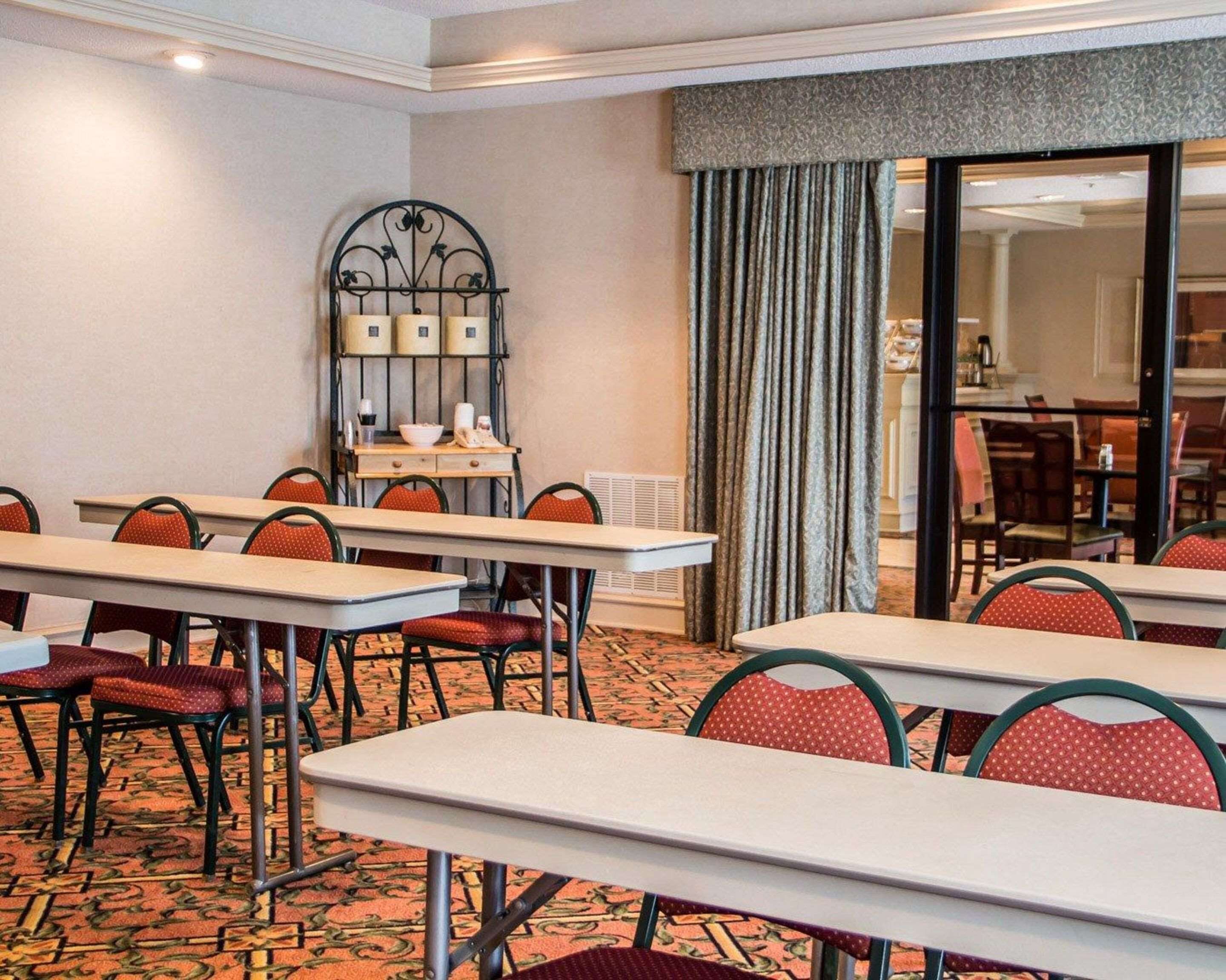 A hotel room with multiple tables and chairs, a decorative metal wall piece, and a large window with curtains.