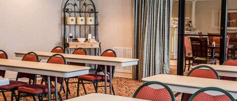 A hotel room with multiple tables and chairs, a decorative metal wall piece, and a large window with curtains.