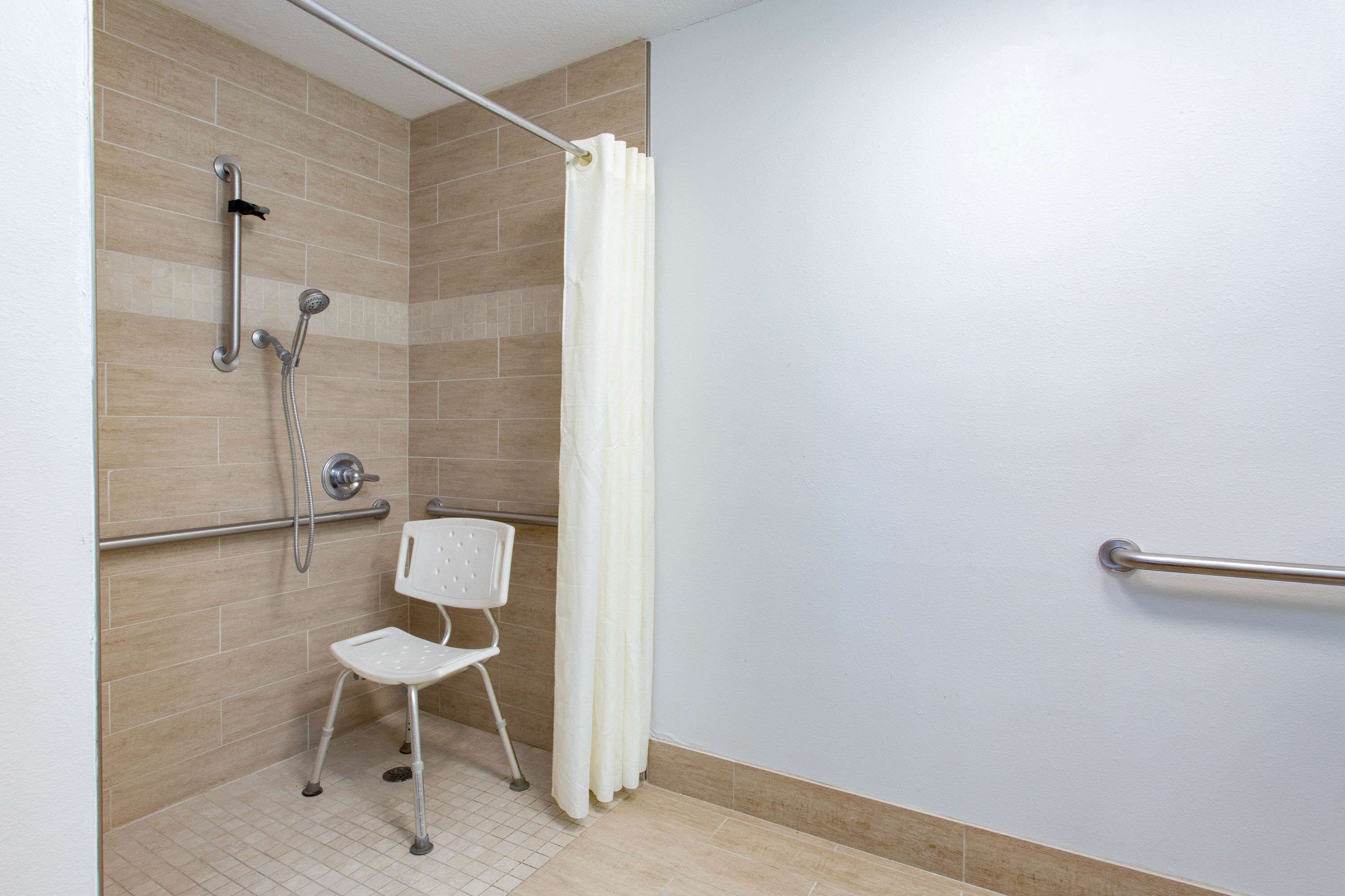 Zona de ducha con una silla blanca, barras de apoyo y un cabezal de ducha.