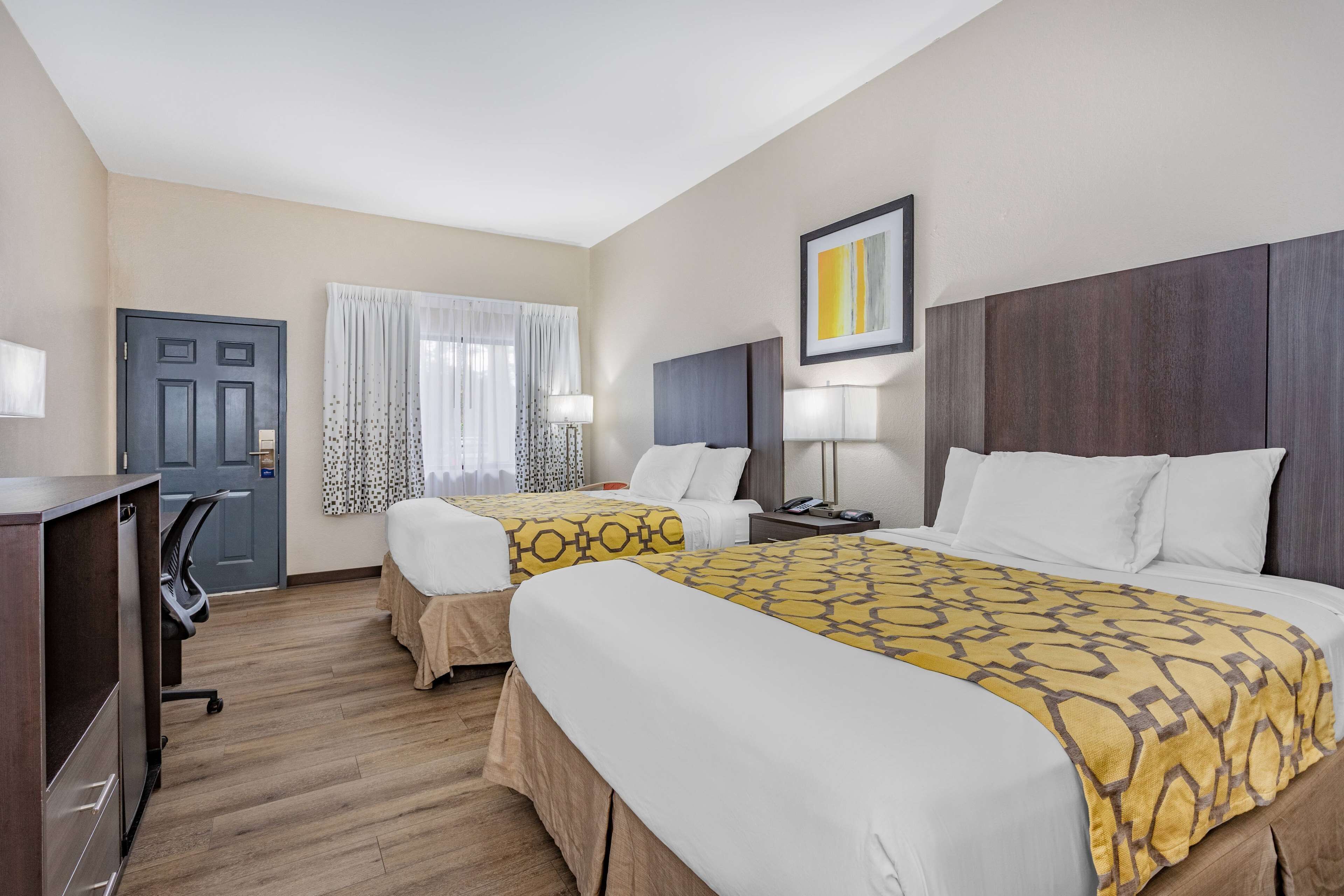 A hotel room with two beds, a desk, a chair, a door, and a window with curtains.