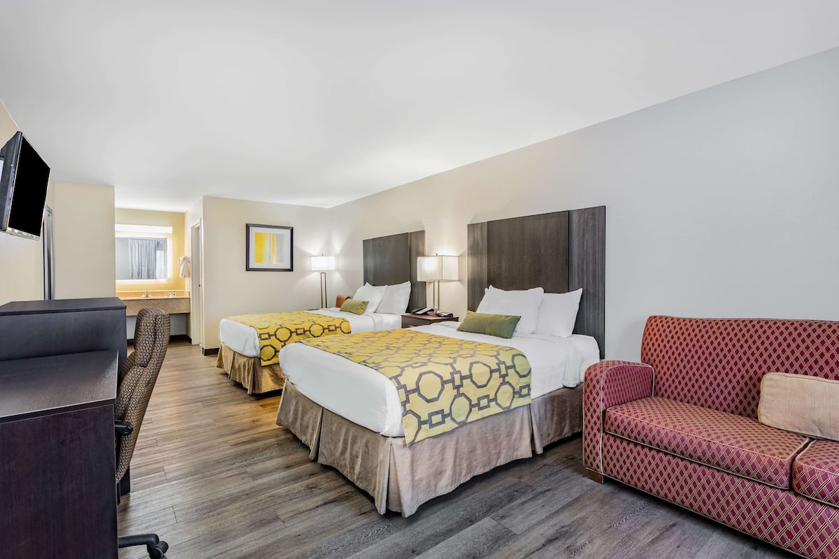 Une chambre d’hôtel avec deux lits, un bureau, un canapé rouge et une télévision.