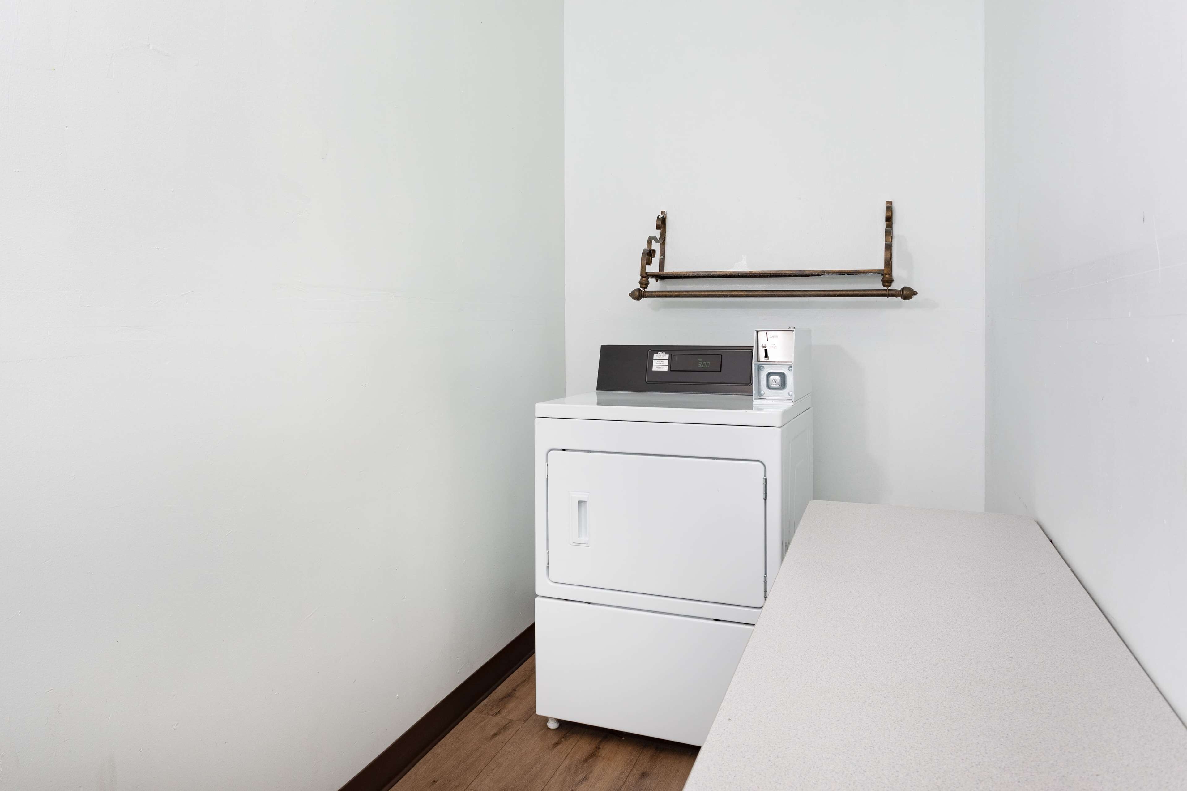 Een kleine wasruimte met een witte wasmachine en droger, een metalen handdoekrek en een houten vloer.