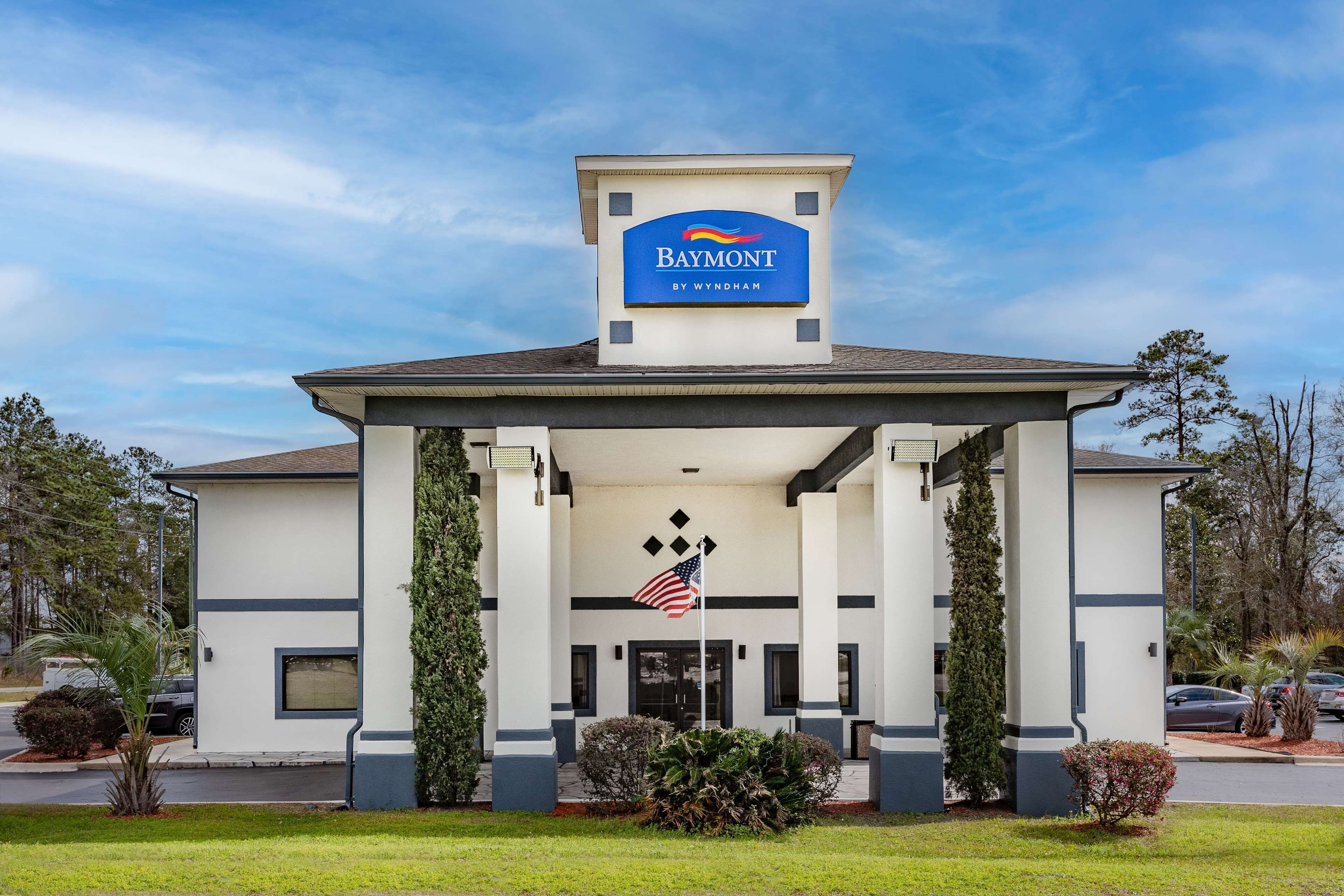 Et Baymont by Wyndham hotel med overdækket indgang, et amerikansk flag og en klar blå himmel.