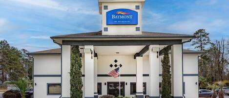 Et Baymont by Wyndham hotel med overdækket indgang, et amerikansk flag og en klar blå himmel.