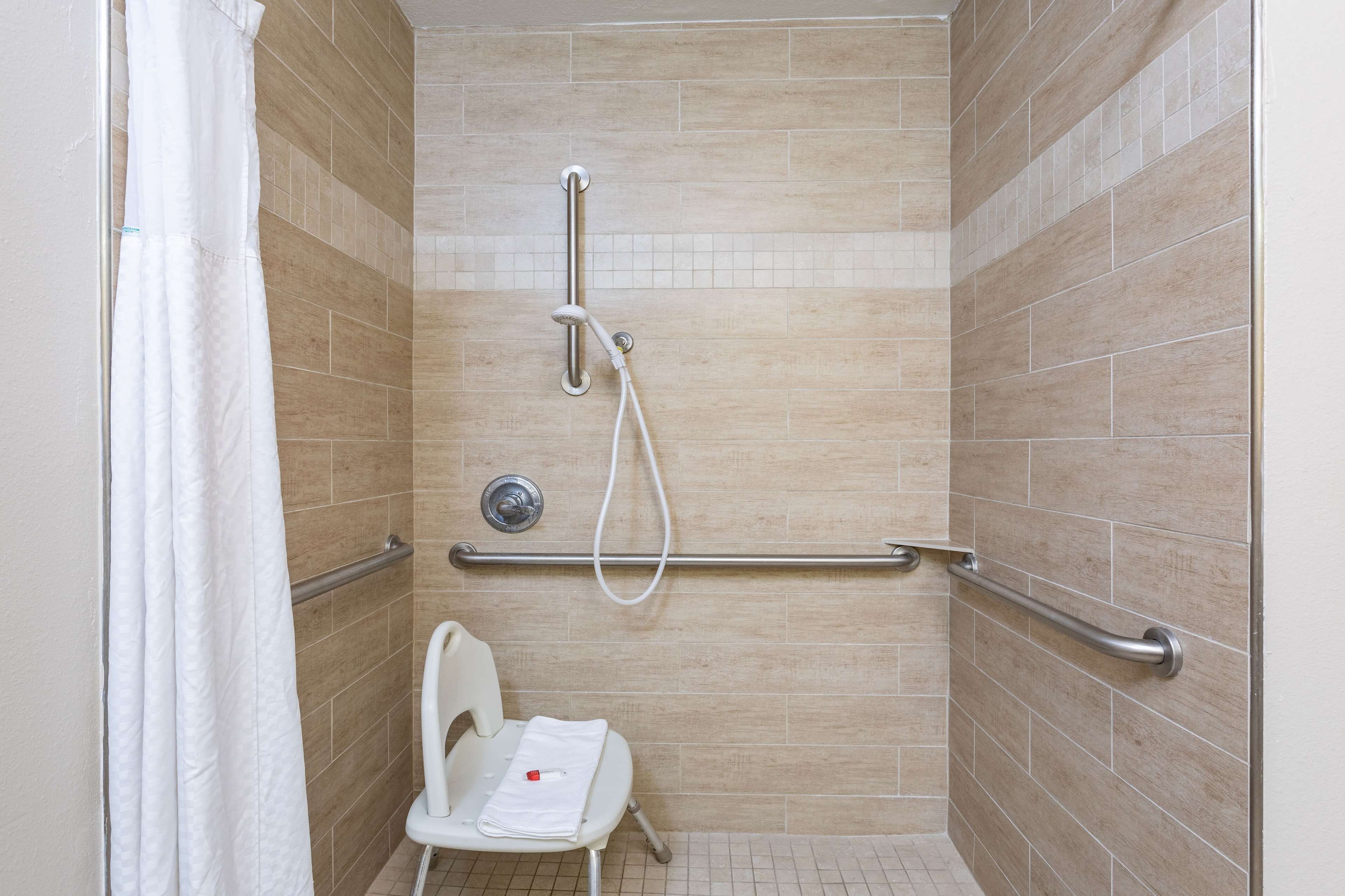 A shower area with beige tiles, a white chair, and a grab bar.