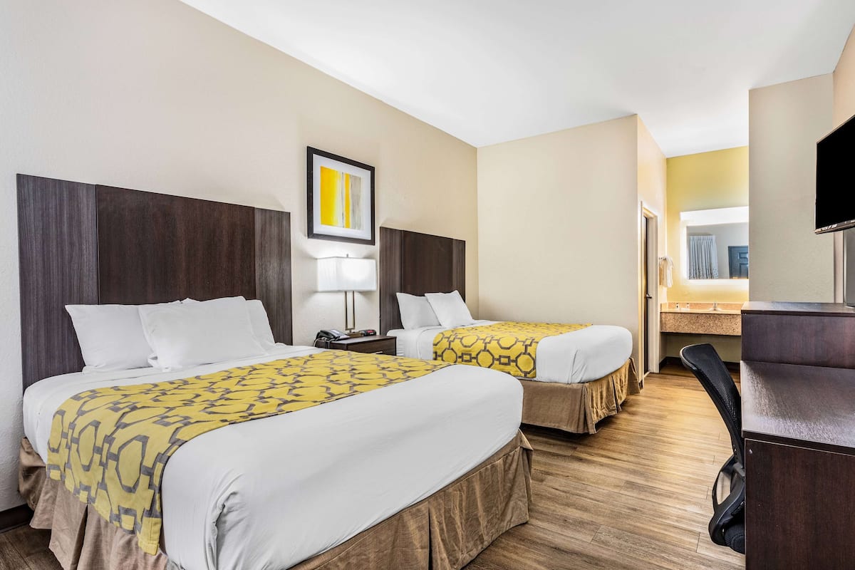 Une chambre d’hôtel avec deux lits, un bureau, une chaise, une télévision et une salle de bain visible à travers une porte ouverte.