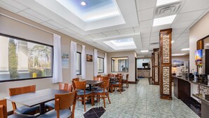 A hotel dining area with tables and chairs, a kitchen area, and a view through the window.