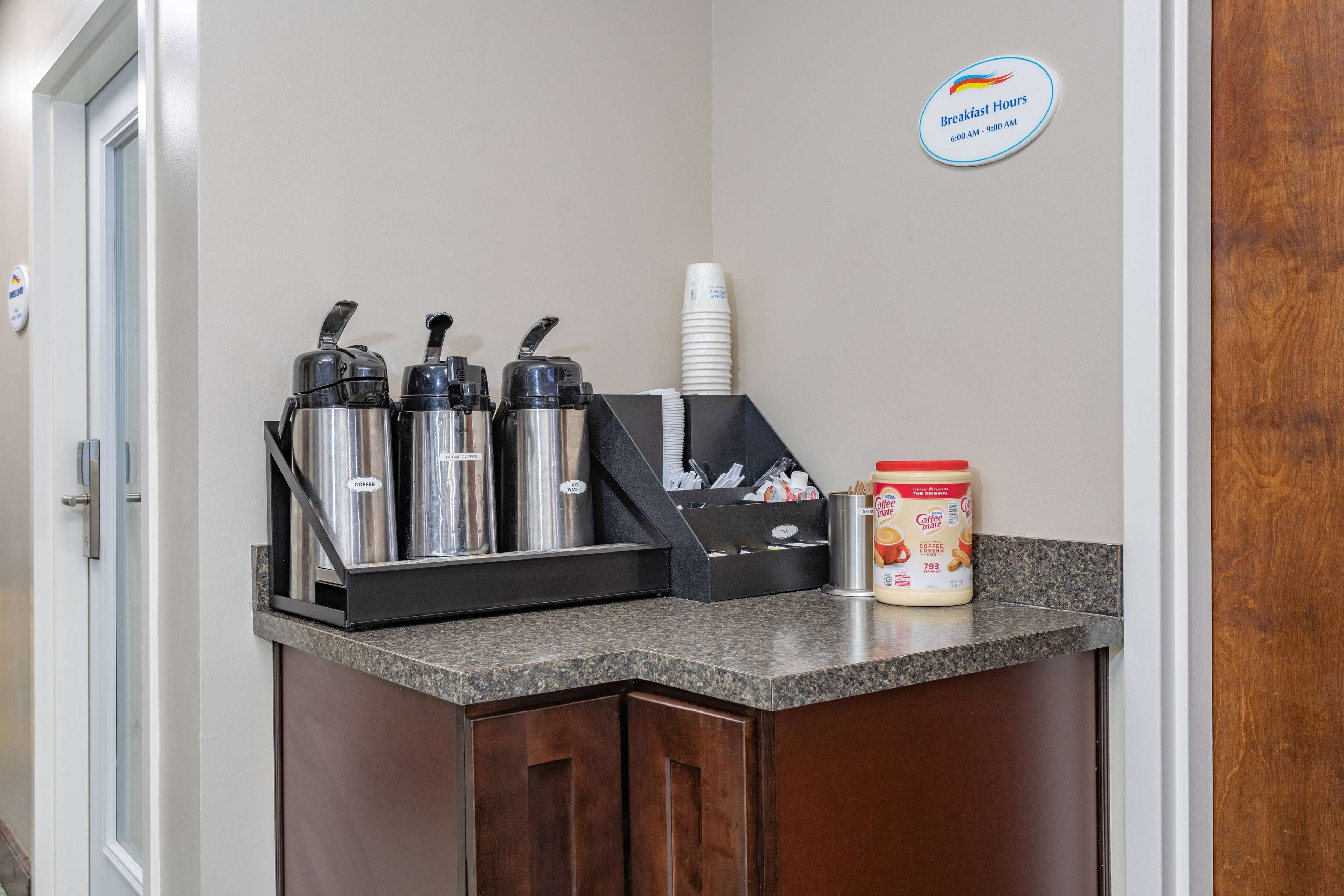 Ein Frühstücksbereich mit Kaffeeautomaten, Einwegbechern und einem Behälter mit Kaffeerahm.