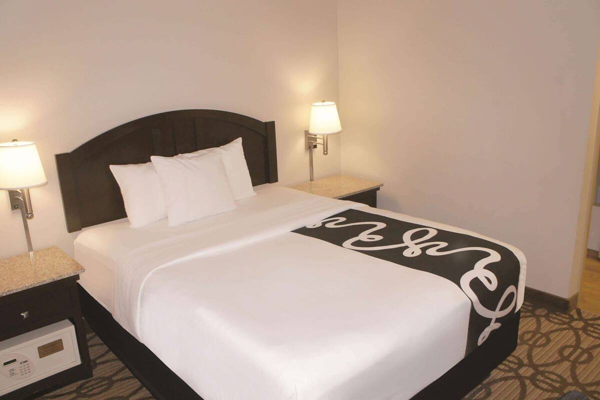 A hotel room with a bed, two bedside lamps, a nightstand, and a control panel.