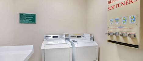 Une buanderie équipée de deux machines à laver et deux sèche-linge, d’un panneau indiquant les règles d’utilisation de la buanderie pour les clients, ainsi que d’un distributeur de savon, d’eau de Javel et d’adoucissant.