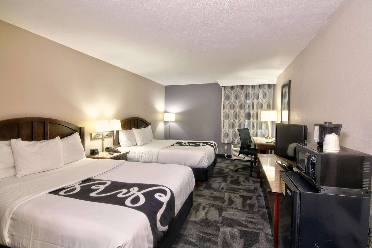 A hotel room with two beds, a desk with a computer, a TV, and a coffee maker.