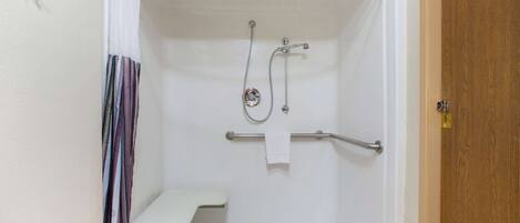 A walk-in shower with a bench, grab bars, and a showerhead.